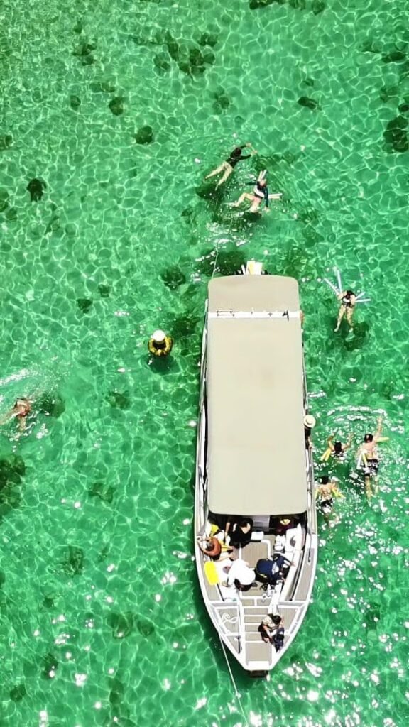 Uma foto de dentro de uma lancha, mostrando a proa cortando o mar calmo, com ilhas verdes no horizonte